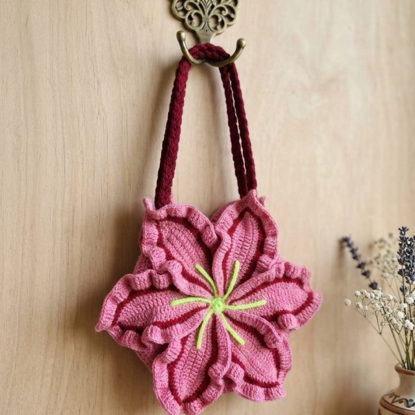 Pink lily flower crochet bag with maroon braided handles hanging on a hook