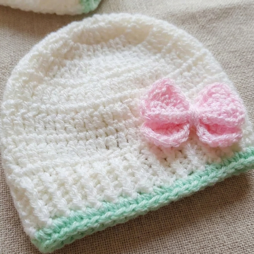 Off-white crochet baby cap with pink bow and mint trim