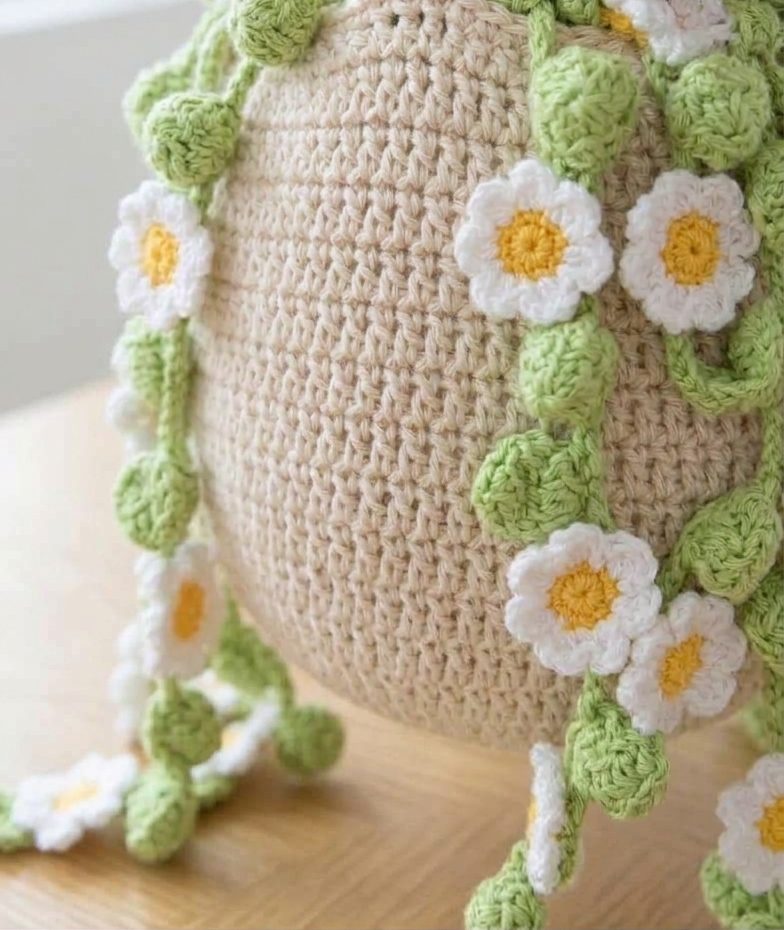 Close-up of crochet daisy flowers and green leaves on bucket bag